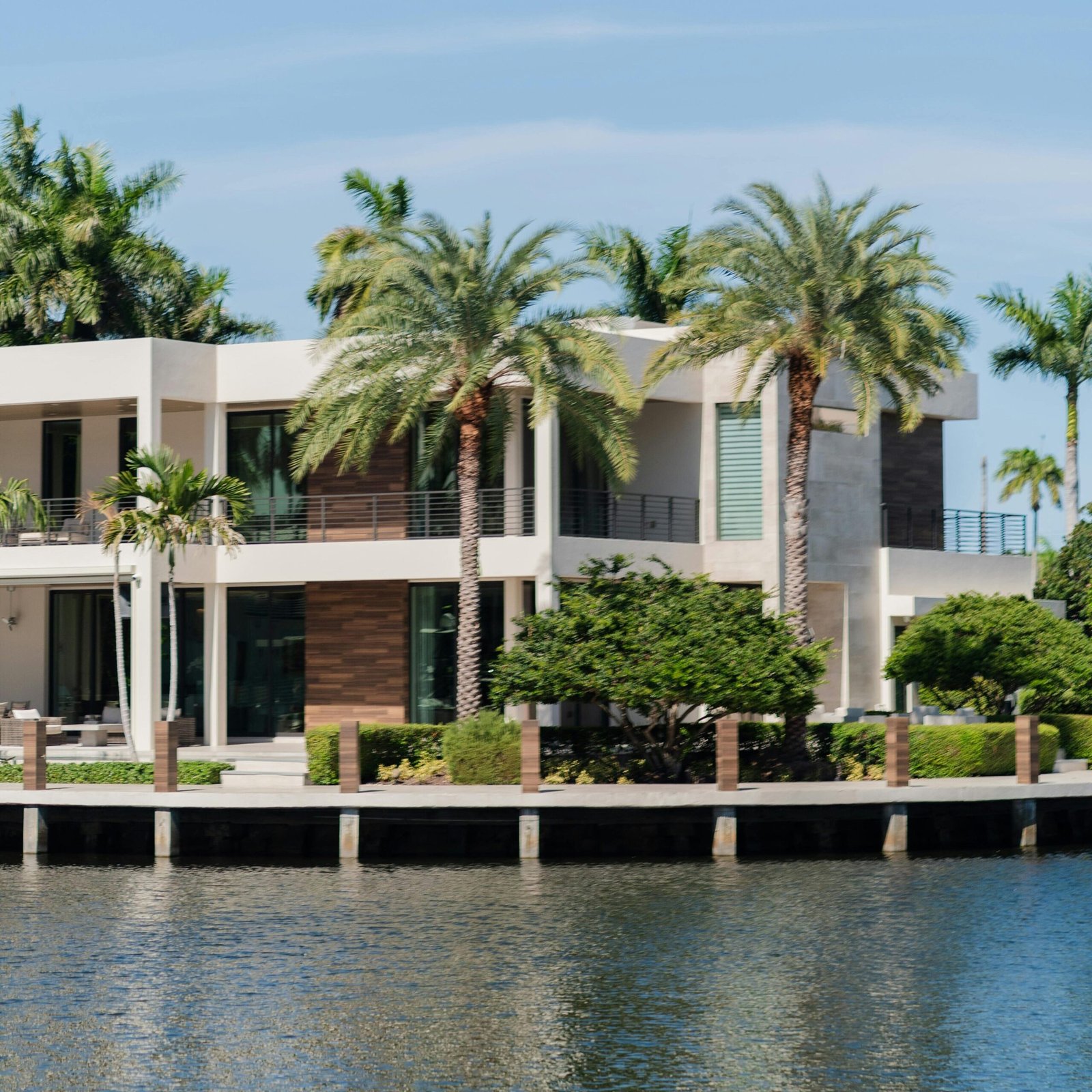 pexels-photo-33397572-33397572 Modern luxury villa by the waterfront surrounded by palm trees, under a clear blue sky.